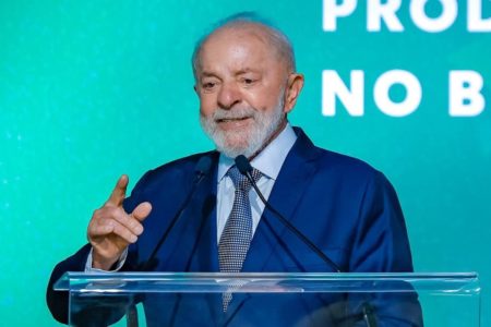 Imagem colorida mostra o presidente Lula sorrindo enquanto fala ao microfone - Metrópoles