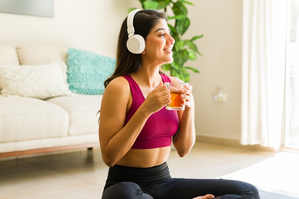 Foto colorida de mulher segurando xícara de chá e com headphones - Metrópoles