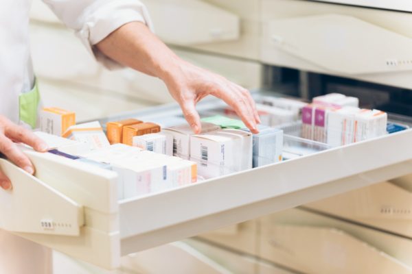 Close up da mão do farmacêutico tirando remédios , medicamentos da gaveta. Fármacia. Metrópoles