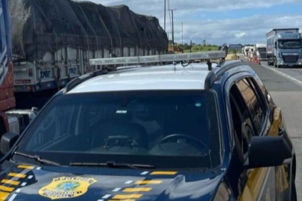 Imagem colorida mostra viatura da Polícia Rodoviária Federal em destaque e, no fundo da imagem, aparece a carroceria de um caminhão que era dirigido por caminhoneiro preso por dívida de pensão alimentícia - Metrópoles