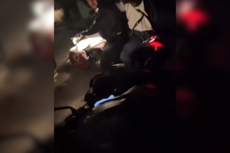 Imagem colorida de dois homens em uma motocicleta abordando outro homem durante a noite - Metrópoles