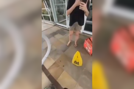 Imagem colorida de uma mulher conversando com um atendente ao celular enquanto é filmada por um motoboy, que foi agredido - Metrópoles