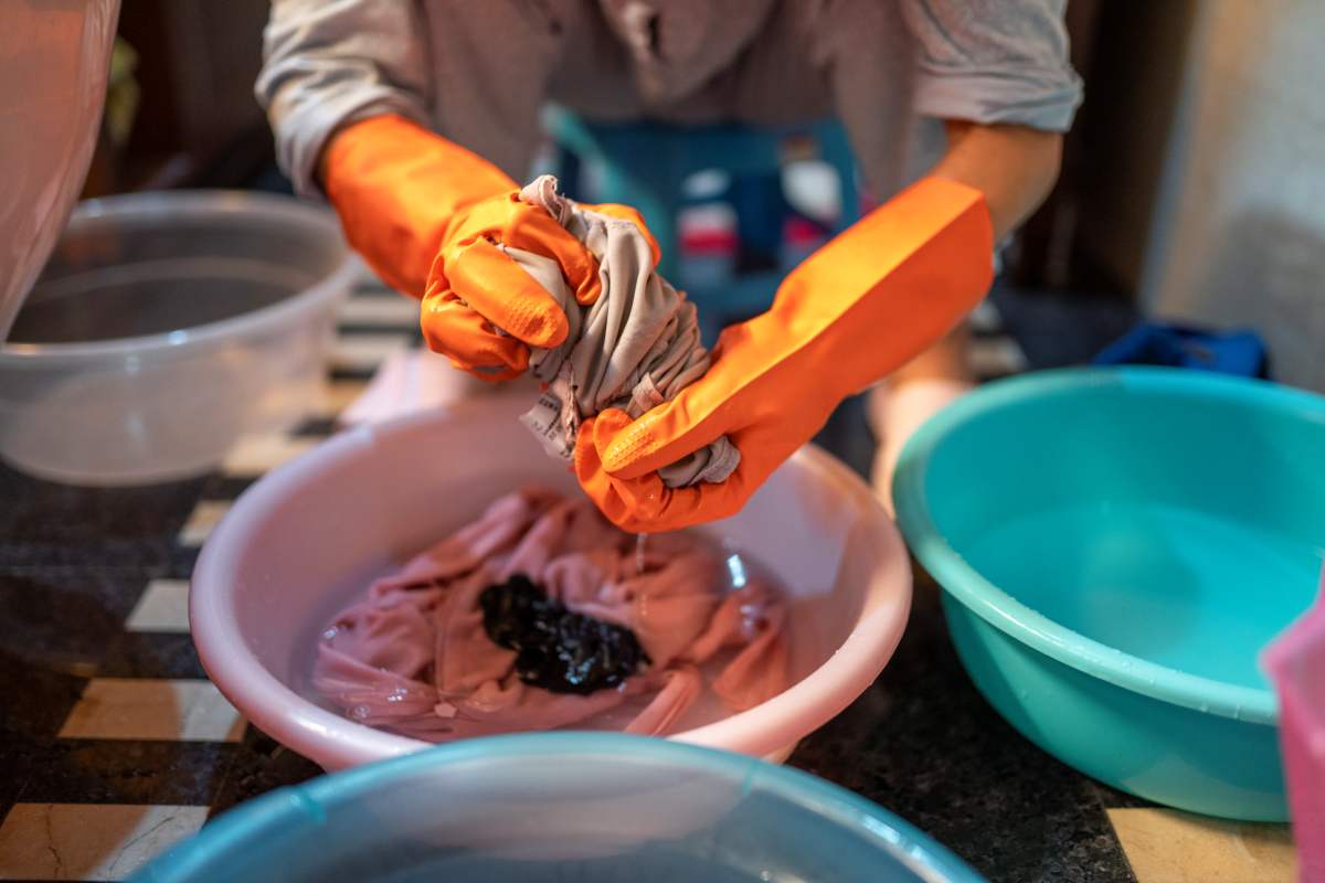 A imagem mostra uma pessoa usando luvas de borracha para lavar roupas. 