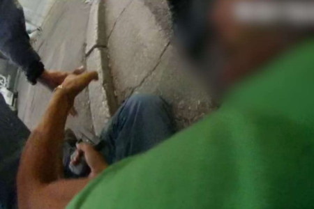 Imagem colorida de homem no chão com arma na mão. Metrópoles