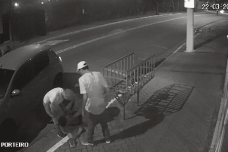 Imagem de uma câmera de segurança mostra três homens agredindo e apontando uma arma no rosto de outro jovem derrubado na calçada - Metrópoles