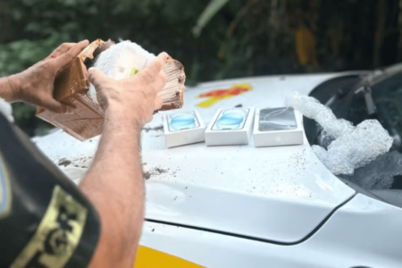 Imagem colorida de um policial averiguando celulares escondidos por motoboy - Metrópoles