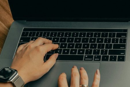 Imagem colorida mostra teclado de notebook com duas mãos femininas digitando - Metrópoles