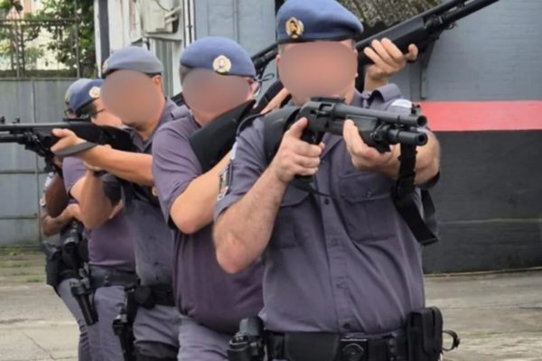 Quatro policiais militares, fardados, enfileirados e em posição ostensiva, mirando cada qual uma arma para o lado oposto do outro - Metrópoles